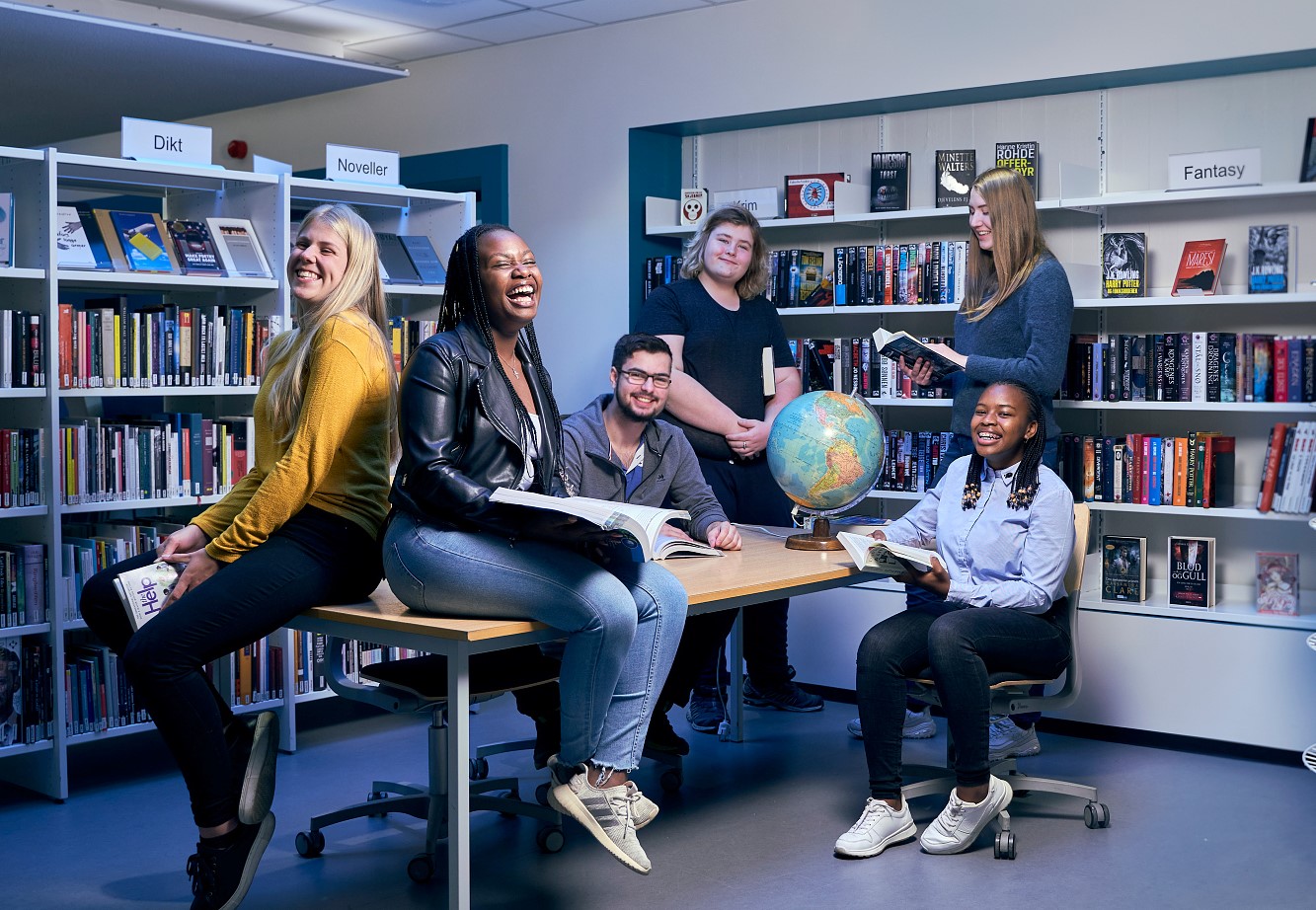 Seks ungdommer i et bibliotek. En globus står på et bord.