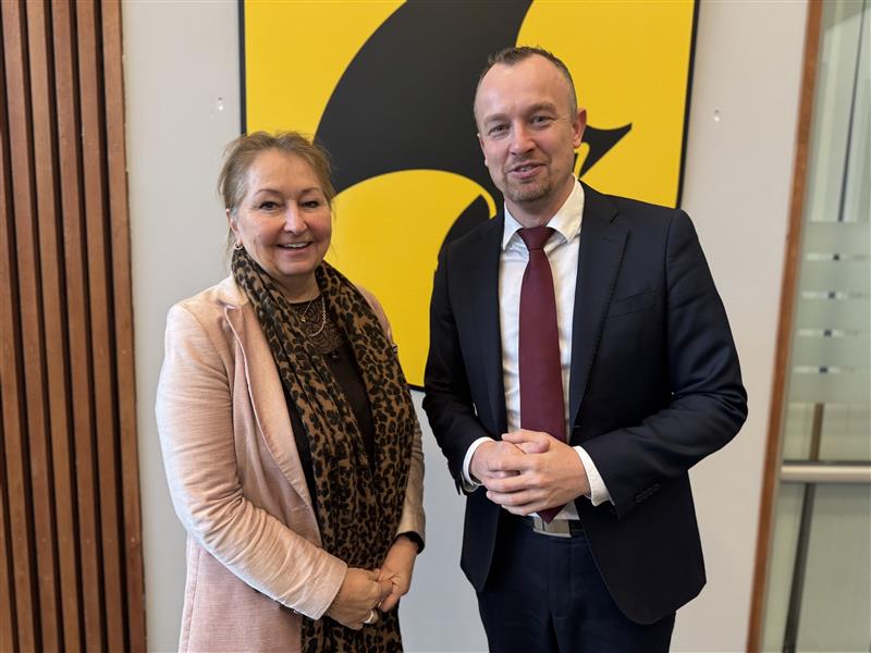 Deler av fronten av et bygg med logoen til Telemark fylkeskommune og en gul buss som er på vei til å passere bygget.