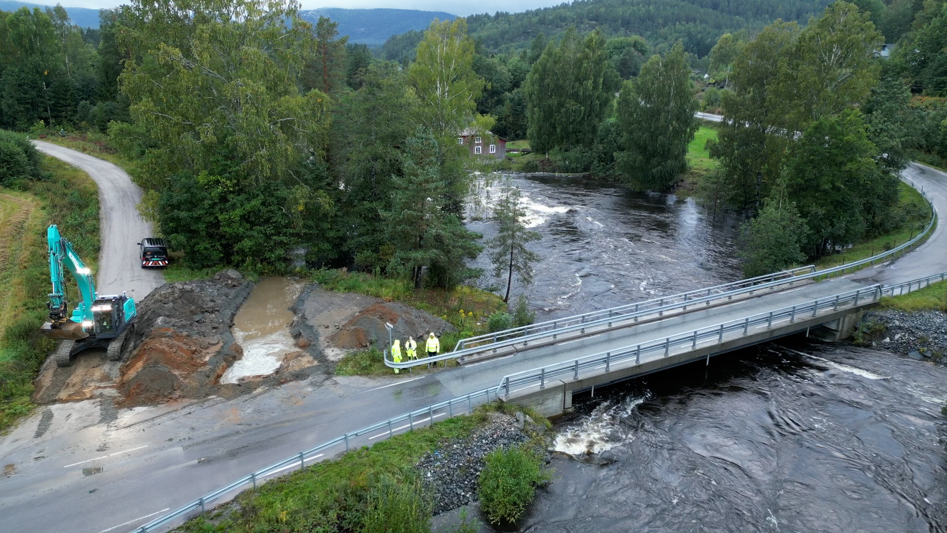 Solberg bru midt i bildet, med elv med høy vannstand under. Til venstre gravemaskin og nygravd grøft.