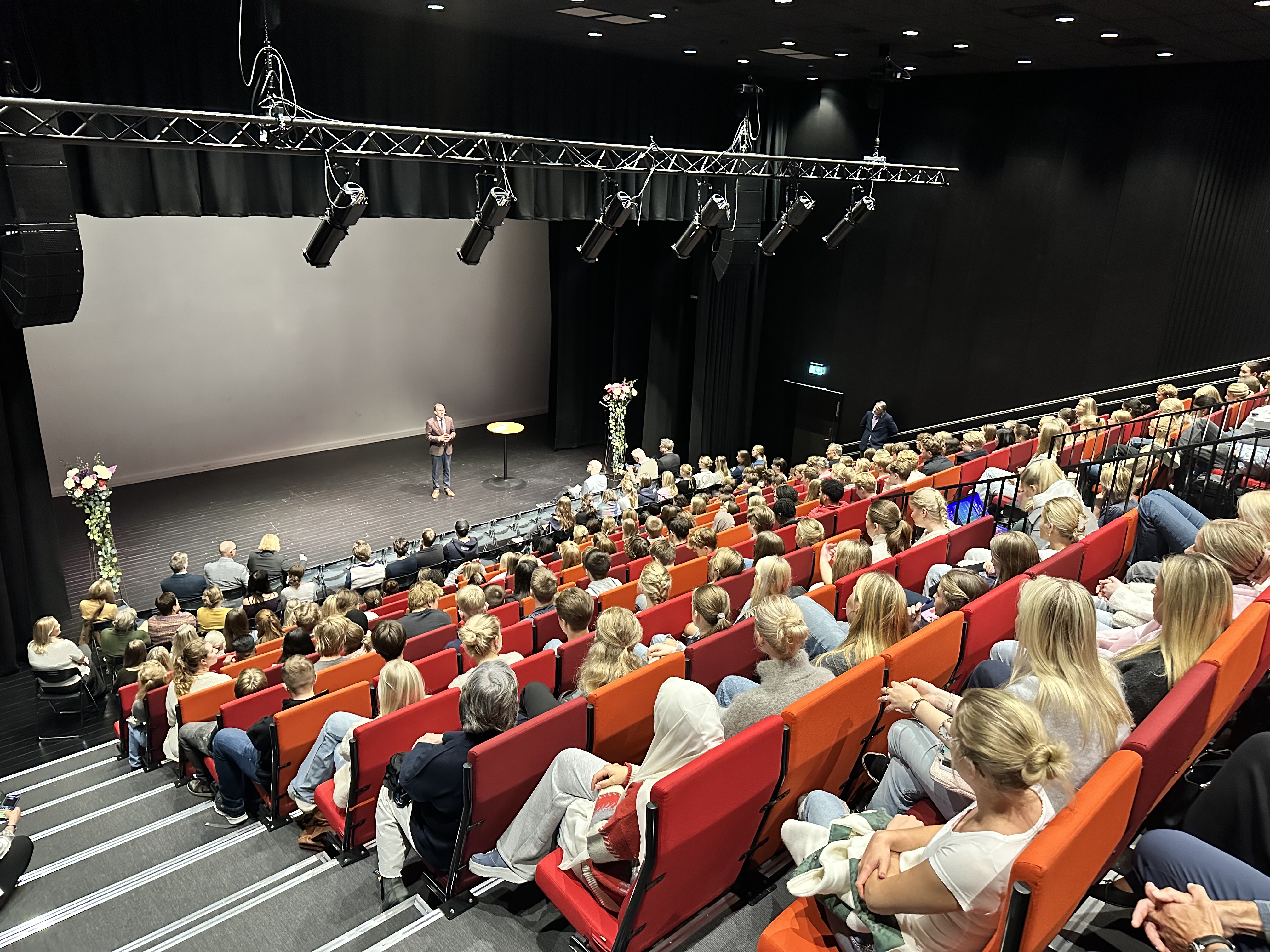 Utenriksministeren står på en scene og prater foran en sal full av lærere og elever på Skien videregående skole.