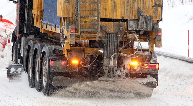 Strøbil som strør fastsand over en isete vei.