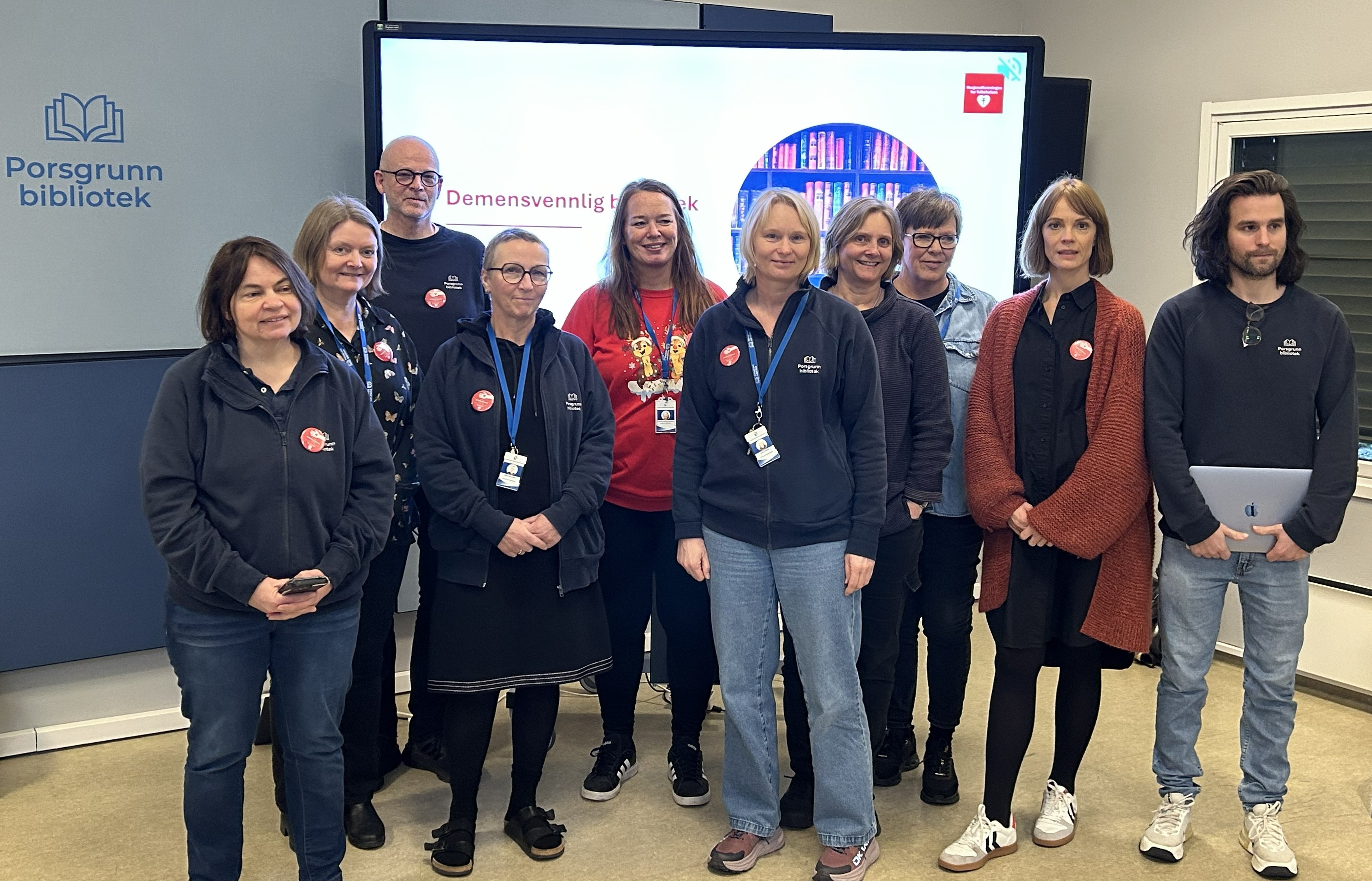 Ti personer står foran en skjerm hvor det står Demensvennlig bibliotek
