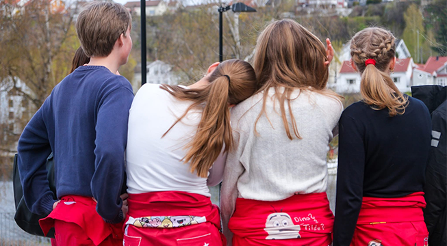 Gruppe med ungdommer i russeklær som står med ryggen til.