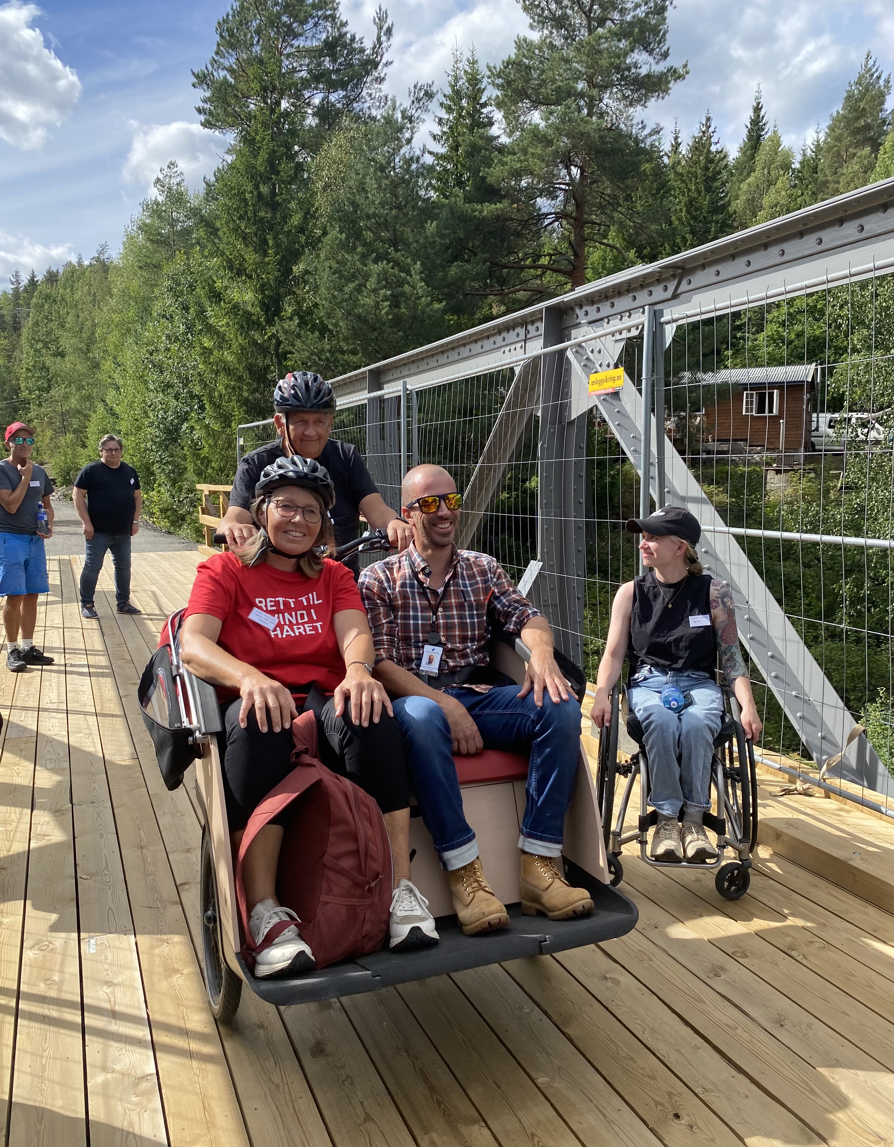 Bilde av en syklist med to passasjerer på setet foran styret på sykkelen