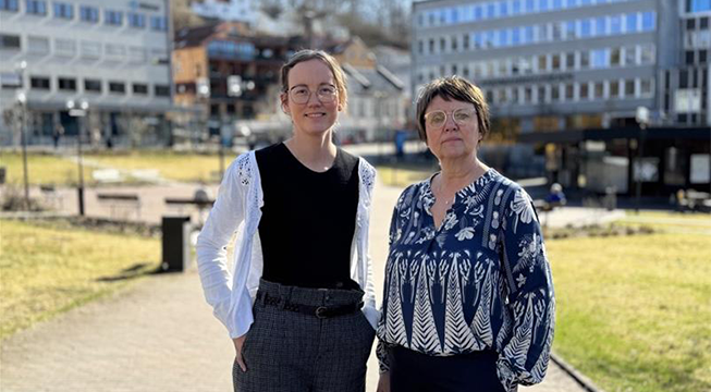 To damer som står i en park og ser mot kamera