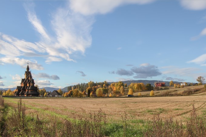 Bilde som viser åker i forgrunn og Heddal stavkirke og gårdsanlegg i bakgrunnen.
