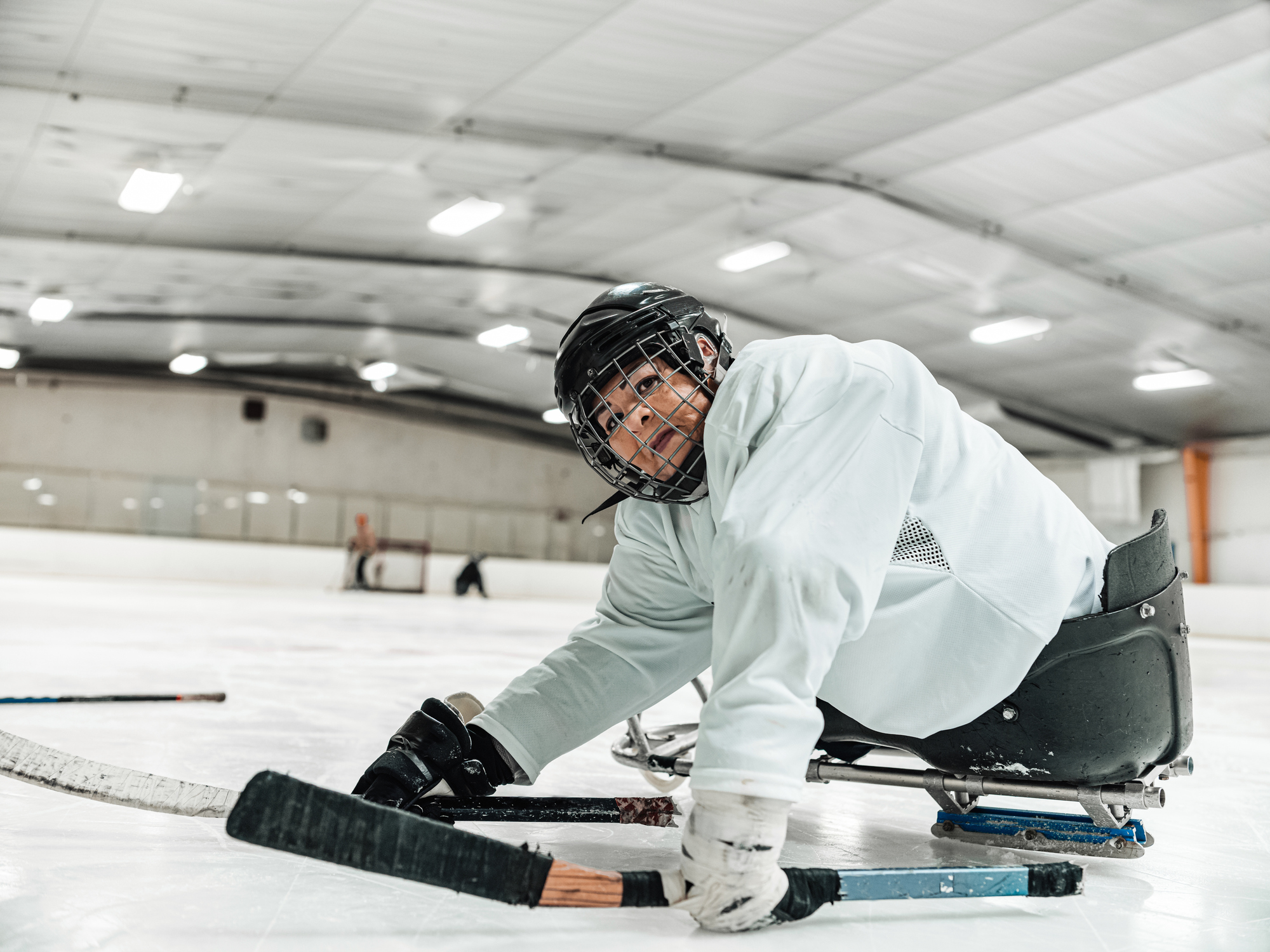 Person som sitter på en parahockeykjelke i fullt hockeyutstyr.