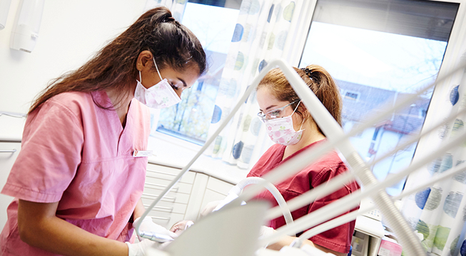 To kvinner med helseuniform og munnbund som jobber i en tannklinikk