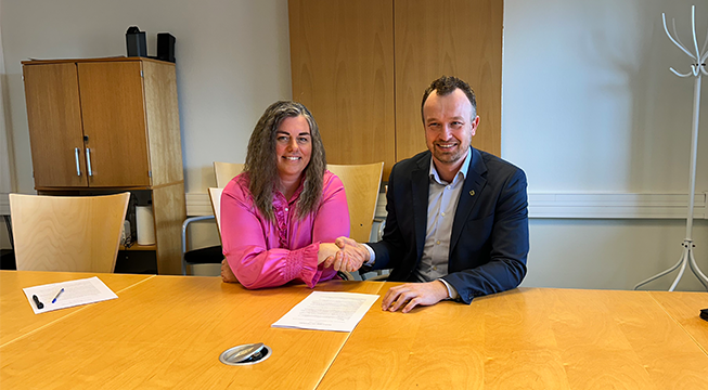 Kvinne i rosa skjorte og man i dress som tar hverandre i hånden etter å ha undertegnet en partnerskapsavtale om Fensfeltet.