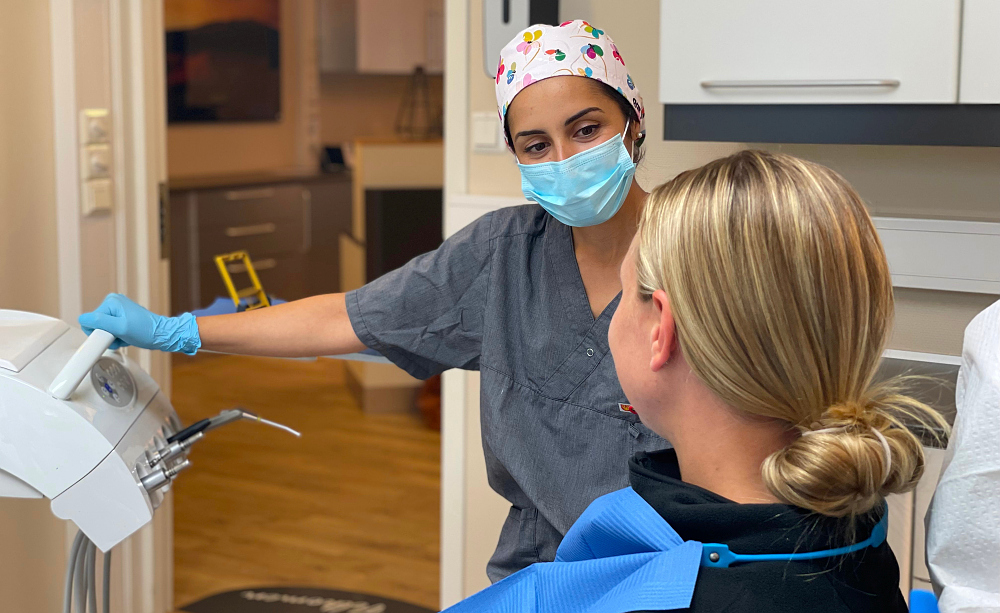 Kvinne med munnbind og helsetøy som ser på en jente som sitter i en stol